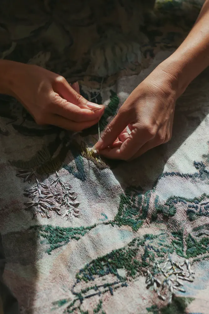 Close-up of Coco Brun’s hands embroidering a landscape tapestry
